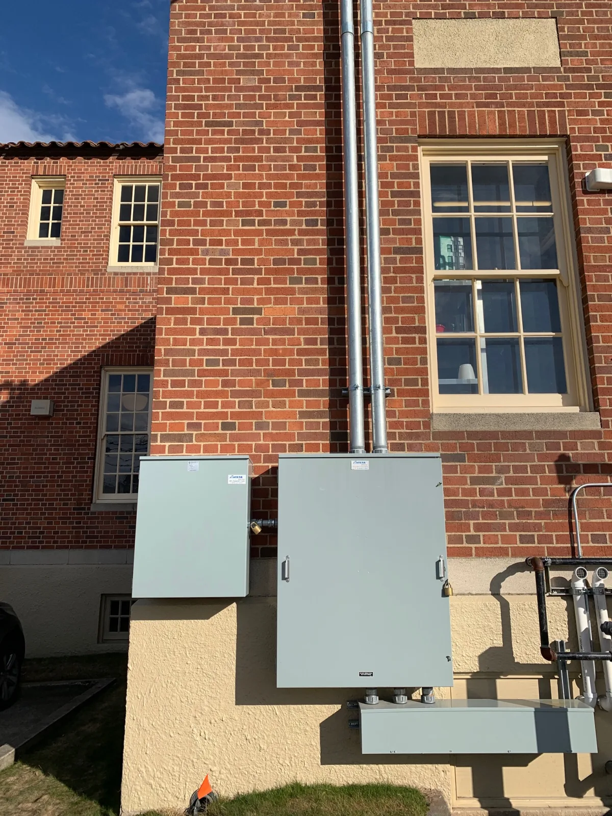 Two service enclosures and a conduit riser mounted on the restored brick exterior at golden hour