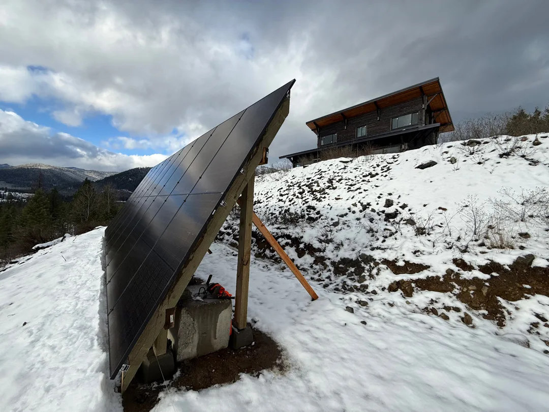 Ground-mount solar array on a snowy Montana hillside beside the home